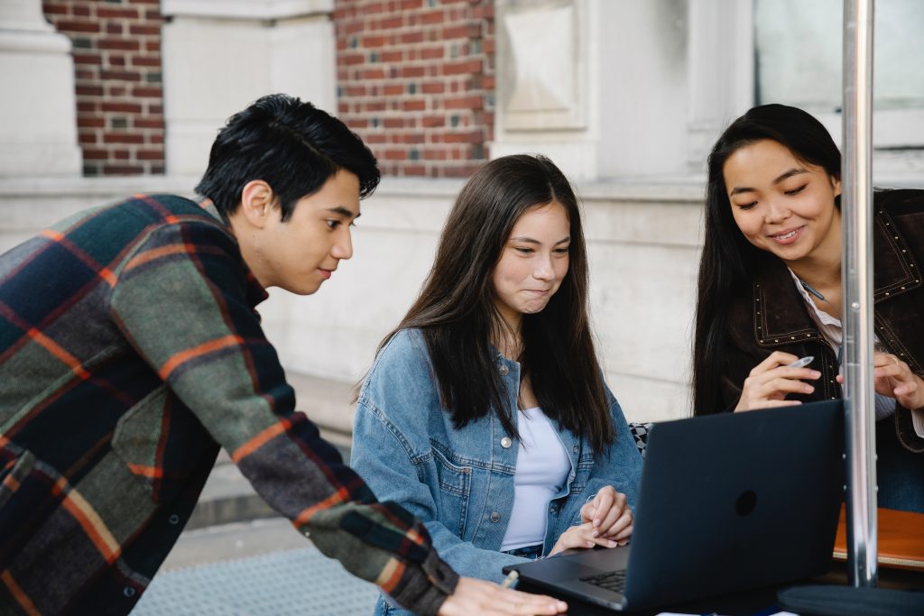 A group of friends viewing a laptop computer screen together outside.