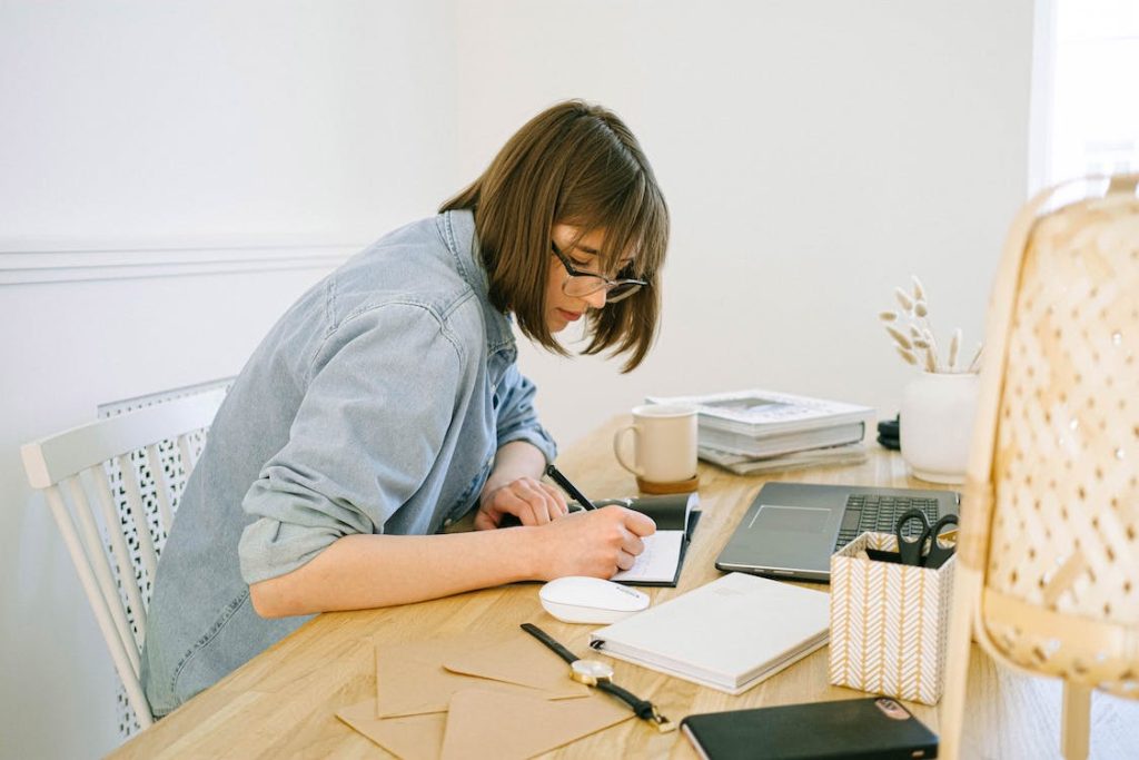 A woman writing in a notebook at a desk to prepare a new article for her WordPress blog.